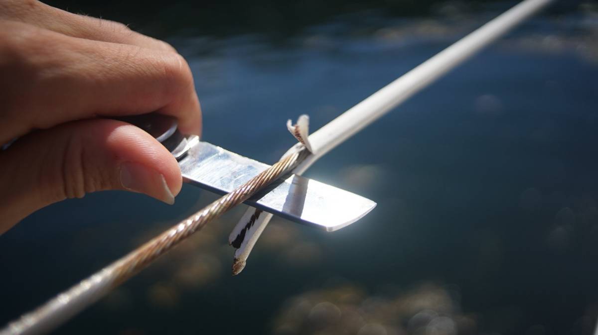 a hand holding a knife, stripping away a plastic covering from a set of lifelines