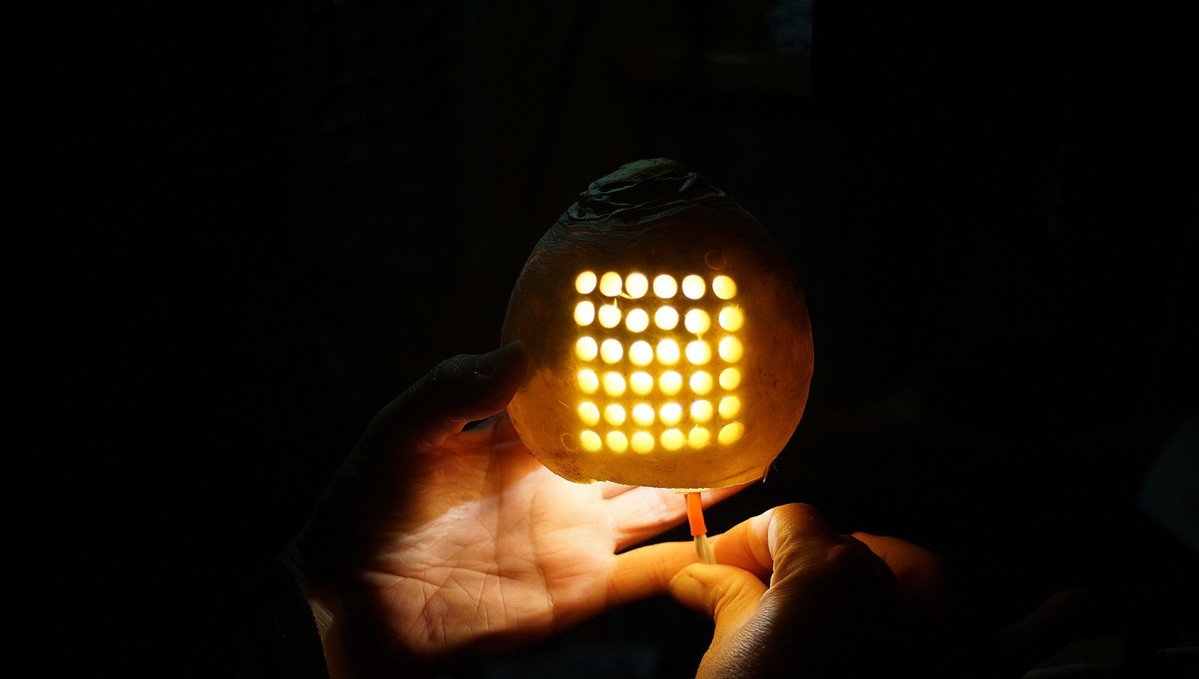 a photo of a hand holding a match inside a hollowed out turnip with the 100r logo carved into its front 