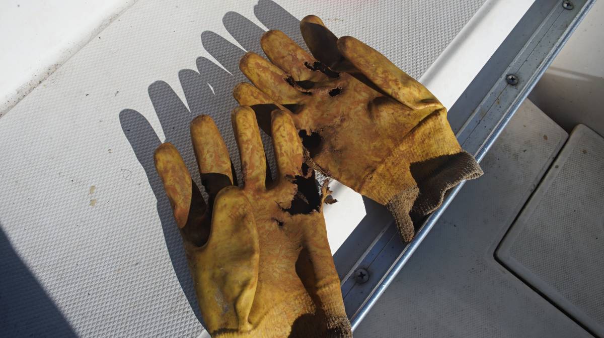 a very worn pair of anchoring gloves, full of holes and covered in rust and dried mud