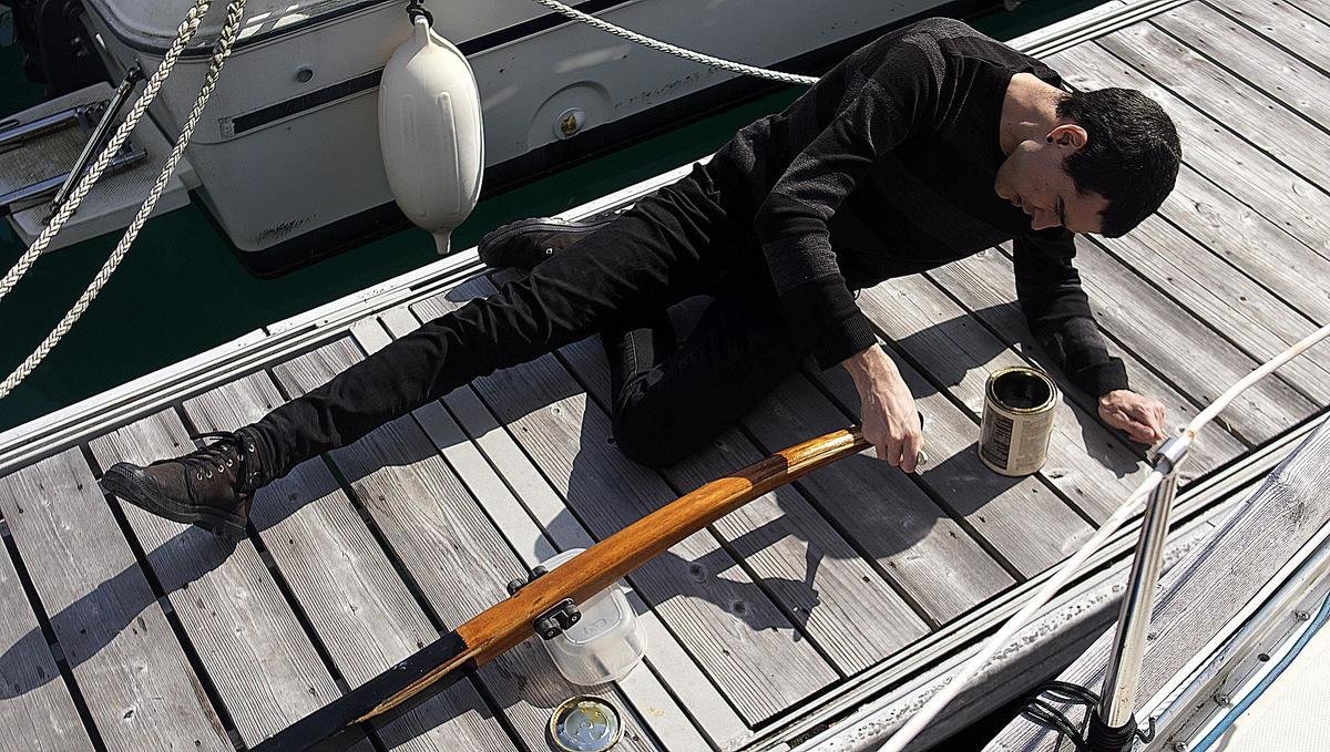 a photo of devine laying on a dock adding a coat of varnish to our wooden tiller