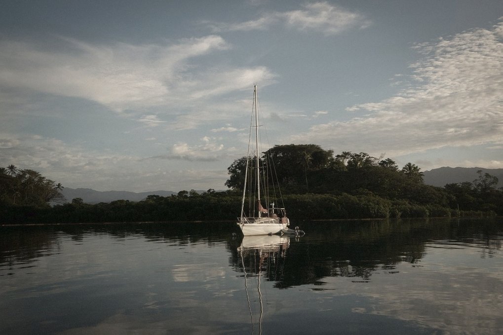 A sailboat is laying on a mooring in a quiet bay under a blue sky