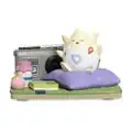 A figure of a Togepi sitting on a cushion on tatami flooring, with a radio and three items, including a Rage Candy Bar, next to it.