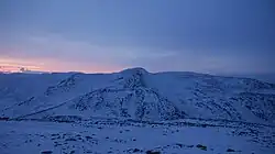 Snow-covered mountains. The whole view appears tinted blue, aide from a faint pink glow on the left of the horizon, which is the sun at its peak.
