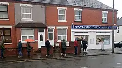 A line of people waiting on the sidewalk of a street, each standing at least 6 feet apart