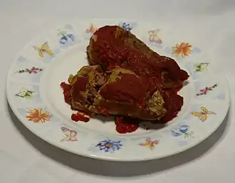 Two turkey and barley cabbage rolls in tomato sauce served on a dinner plate.