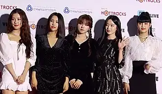 Four women dressed in black outfits. The third woman from the left is holding a small trophy