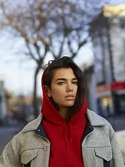 Dua Lipa on the street wearing a red hoodie and a glittery jacket.