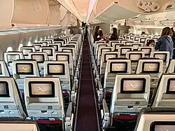Inside view of an aircraft's Economy Class cabin with television on the back of the seats and overhead lockers on the ceiling