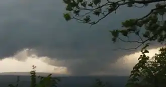 A photo of the tornado as it was on a hill; the tornado itself and the cloud above is visible. The photo is taken from a distance.