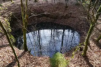 Funnel-shaped hole, flooded, remains of the Croix well.