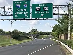 A multilane highway in a suburban area at a split, with two green signs over the road. The sign on the left reads north Interstate 287 to Interstate 78 Netcong Morristown with an arrow pointing to the upper right and the sign on the right reading north U.S. Route 202/U.S. Route&nbsp;206 Pluckemin.