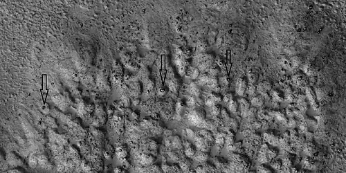 Closer view of ejecta, as seen by HiRISE under HiWish program. Note: Arrows show examples of boulders sitting in pits.