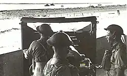 Gunners at 4.7-inch (120&nbsp;mm) gun watching vessels at river mouth. 1943.[gallery 16]