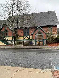 A photo of a building formerly owned by St. John's Episcopal Church, now owned by Arlington Friends of the Drama. This photo depicts the side doors of the building. The righthand door, which is situated below street-level, leads into the theatre's lobby. The lefthand door, up a small flight of stairs, is a side entrance into the theater.