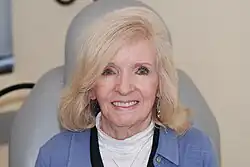 The same 71-year old woman, sitting, facing the camera, and smiling, with no visible tumour.