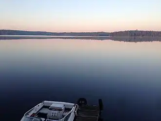 A very calm lake at sunset, showing trees on the far shore