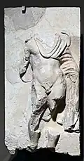 A marble relief of a man wearing a toga; the head is missing, along with parts of all four limbs