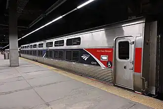 A silver railroad car with a blue stripe over the windows. At one end, an angular red shape covers the stripe.