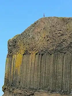 Cliff face showing three layers of rock; the bottom layer is sedimentary rock; the middle layer forms columns, whilst the layer above is blocky in appearance.