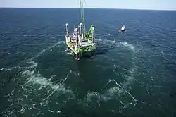 Aerial view of a structure in the sea, surrounded by a circle of lighter patches where bubbles are emerging