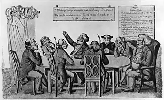 Men sitting around a table. Most of them are muzzled, some are gagged as well, some have blindfolds on, and some have their ears muffled.