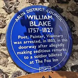 A blue memorial plaque on a wall outside of The Fox Inn at Felpham, West Sussex describing Blake's arrest. It reads "Arun District Council. William Blake 1757 - 1827. Poet, Painter, Visionary was arrested, in 1803, in this doorway after allegedly making seditious remarks to a soldier billeted at The Fox Inn.