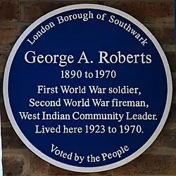 Circular blue plaque, with six lines of text reading "George A. Roberts / 1890 to 1970 / First World War soldier, / Second World War fireman, / West Indian Community Leader / lived here 1923 to 1970". Above those, the text "London Borough of Southwark" and below them, "Voted by the People".