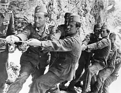 a number of men in SS uniforms and wearing fez headgear straining to pull on a rope.