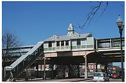 A green station house in a Queen Anne style, with a staircase on the left side leading up to it