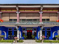 Front façade of a double-storey Oriental-style mansion, coloured in blue and with the upper floor partially concealed by wooden blinds.