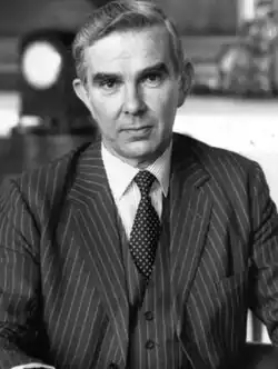 b/w image of middle-aged and impeccably-groomed caucasian male dressed in a charcoal grey 3-piece pinstriped suit