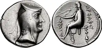 Two sides of a silver coin. The one on the left bears the imprint of a man's head, while the one on the right a sitting individual.