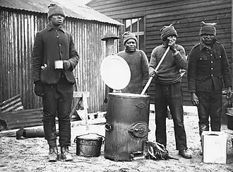 Cooking in a labour camp, Western Front, during World War I. This photograph shows four men cooking and drinking soup from one of the army outside catering boilers. They are all probably members of (4687898545)