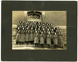 A group portrait of Girl Scouts in Crothersville, Indiana, circa 1945. The girls are gathered in rows and are standing in front of the doors of a brick building.