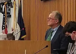 Dan Cronin seated on the dais of the board room. The flags of the United States, the State of Illinois, and County of DuPage are in the background.