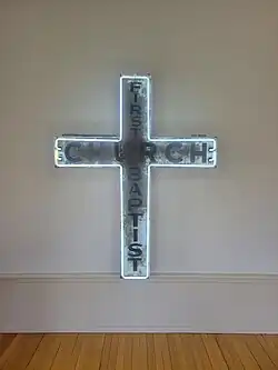 A white neon outlined cross with the word "Church" across the horizontal and "First Baptist" running down the vertical.