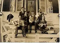 1937 B&W photograph of Donn Reynolds (top left) as "The Yodeling Ranger" seated on steps with his band (Winnipeg, Manitoba, Canada).