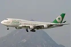 Aircraft in flight. Side view of quad-engine jet with extended landing gear and flaps.