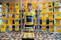Egan Bernal wearing his team kit and yellow jersey standing in front of a museum exhibition of historic yellow jerseys