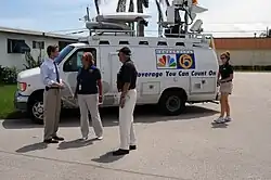A WPTV reporter talks with guests in front of a satellite newsgathering truck bearing the WPTV logo and the slogan "Coverage You Can Count On"