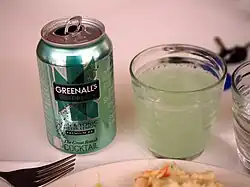 A green soda can next to a glass of green liquid.