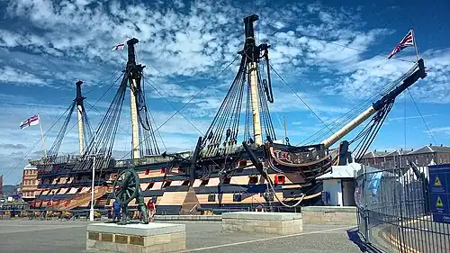 A picture of HMS Victory, the world's oldest commissioned naval ship, situated in Portsmouth's dry dock. The ship itself is missing its figurehead in this photo, but retains its original sails.