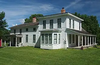 A two-story wooden house with multiple sections, porches, and a bay window