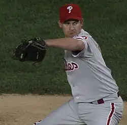 A man wearing a gray baseball uniform and red baseball cap throwing a baseball with his right hand