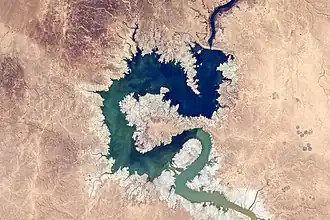 Image 16 Haditha Dam Photograph credit: NASA, Kjell N. Lindgren The Haditha Dam is an earth-filled dam in Iraq, holding back the waters of the Euphrates to create Lake Qadisiyah. The area around Haditha is very arid, with a hot desert climate; the annual precipitation is about 127 millimetres (5 in), mainly occurring during the winter. This photograph, taken from the International Space Station in November 2015, shows the reservoir at a low water level, surrounded by an expanse of dry lakebed; the Haditha Dam is visible near the top of the image. Lake Qadisiyah has a maximum water-storage capacity of 8.3 cubic kilometres (2.0 cu mi) and a maximum surface area of 500 square kilometres (190 sq mi). The associated hydroelectric power station is capable of generating 660 megawatts of electricity, and outlets at the foot of the dam can discharge 3,000 cubic metres (110,000 cu ft) of water per second for irrigation.