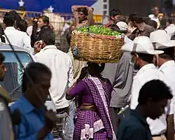 A woman carrying a basket full of vegetables on her head in K R Market, Bangalore, India