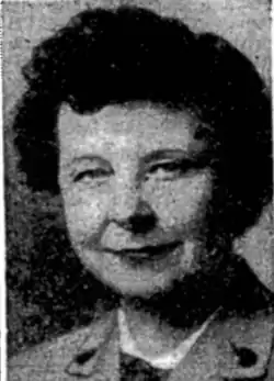 A white woman with fair skin and dark hair wearing a Girl Scout of USA adult uniform with metal buttons