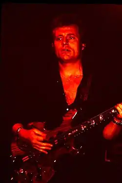 A red tinged photograph of John Paul Jones playing a bass guitar