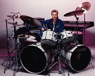 Promotional photo of John Robinson sitting behind a Yamaha drum kit in 1985
