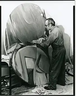 man in overalls standing by artwork